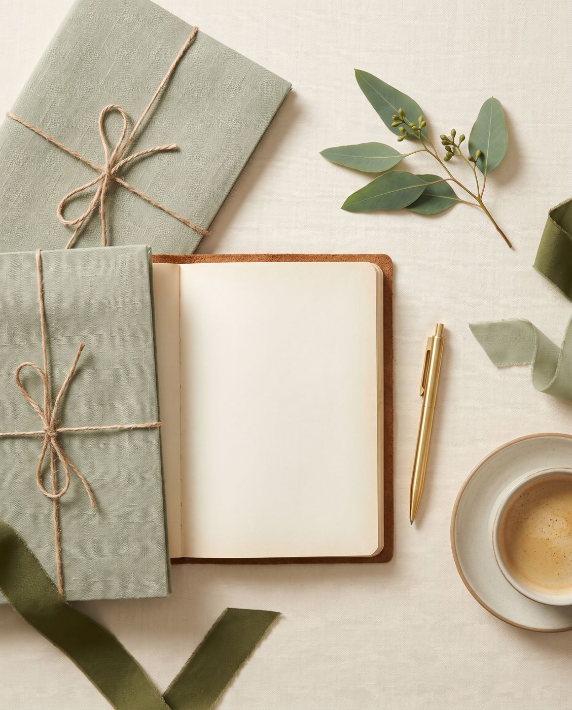 Sage notebooks, a pen and coffee laid out on a linen desk